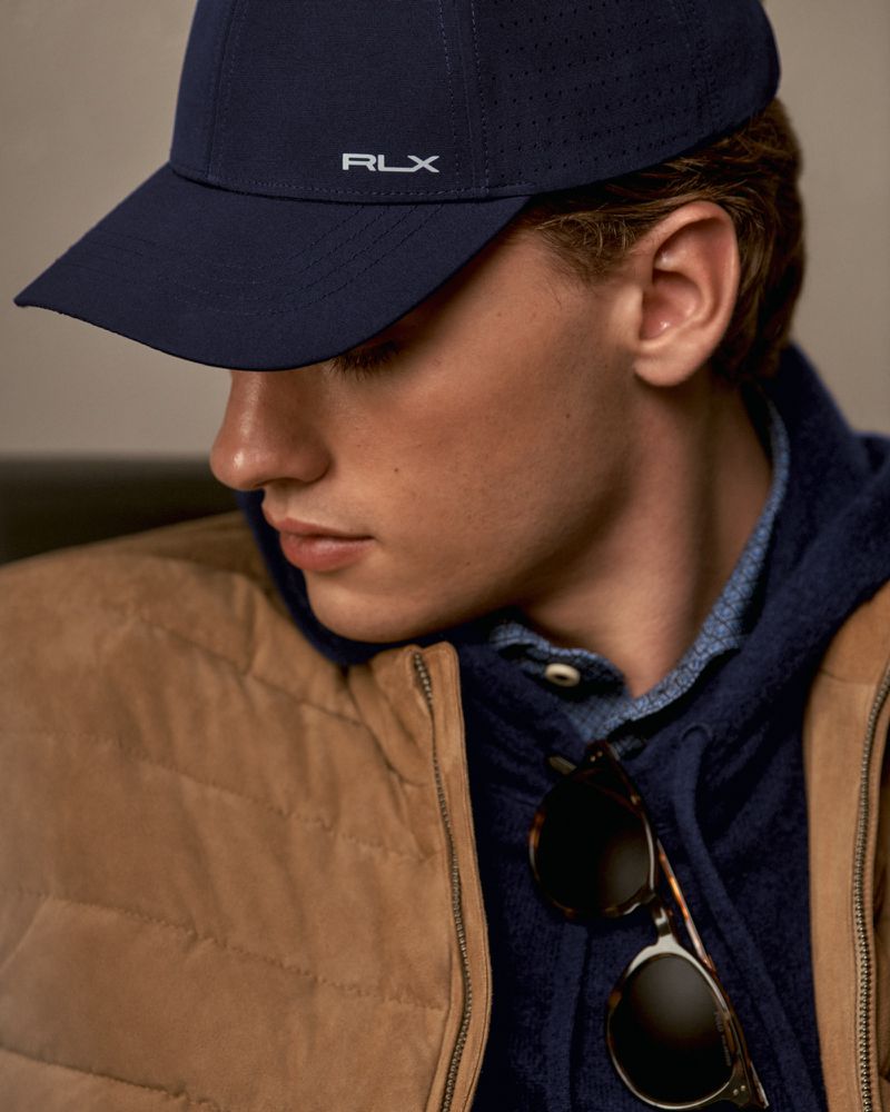 Man in a navy RLX ball cap and tan puffer vest poses in a medium shot, showcasing fashion and casual wear for an apparel advertisement.