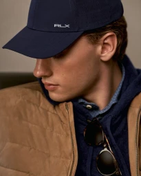 Man wearing a navy baseball cap and tan vest over a blue hoodie with sunglasses