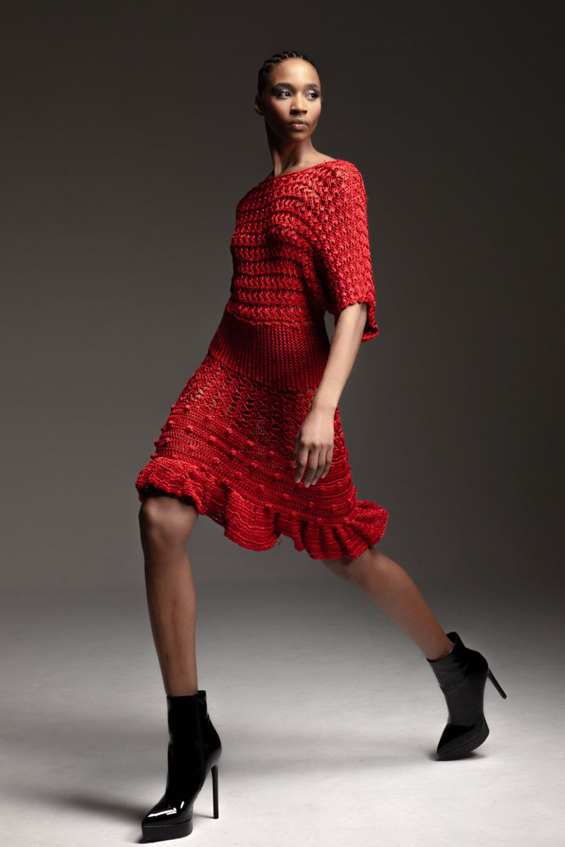 Fashionable African American woman in a red textured short dress and black patent leather ankle boots poses in a studio setting.