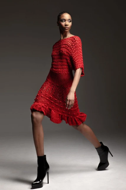Fashionable African American woman in a red textured short dress and black patent leather ankle boots poses in a studio setting.