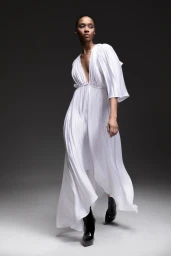 Model in a flowing white dress and black boots against a neutral grey studio background for Frederick Anderson Pre Fall 2024