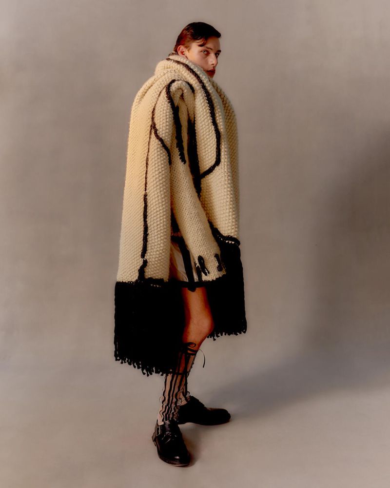 Fashion shot of adult model posing in a cream-colored knit wrap coat with black trim, matching skirt, and black striped sheer socks.