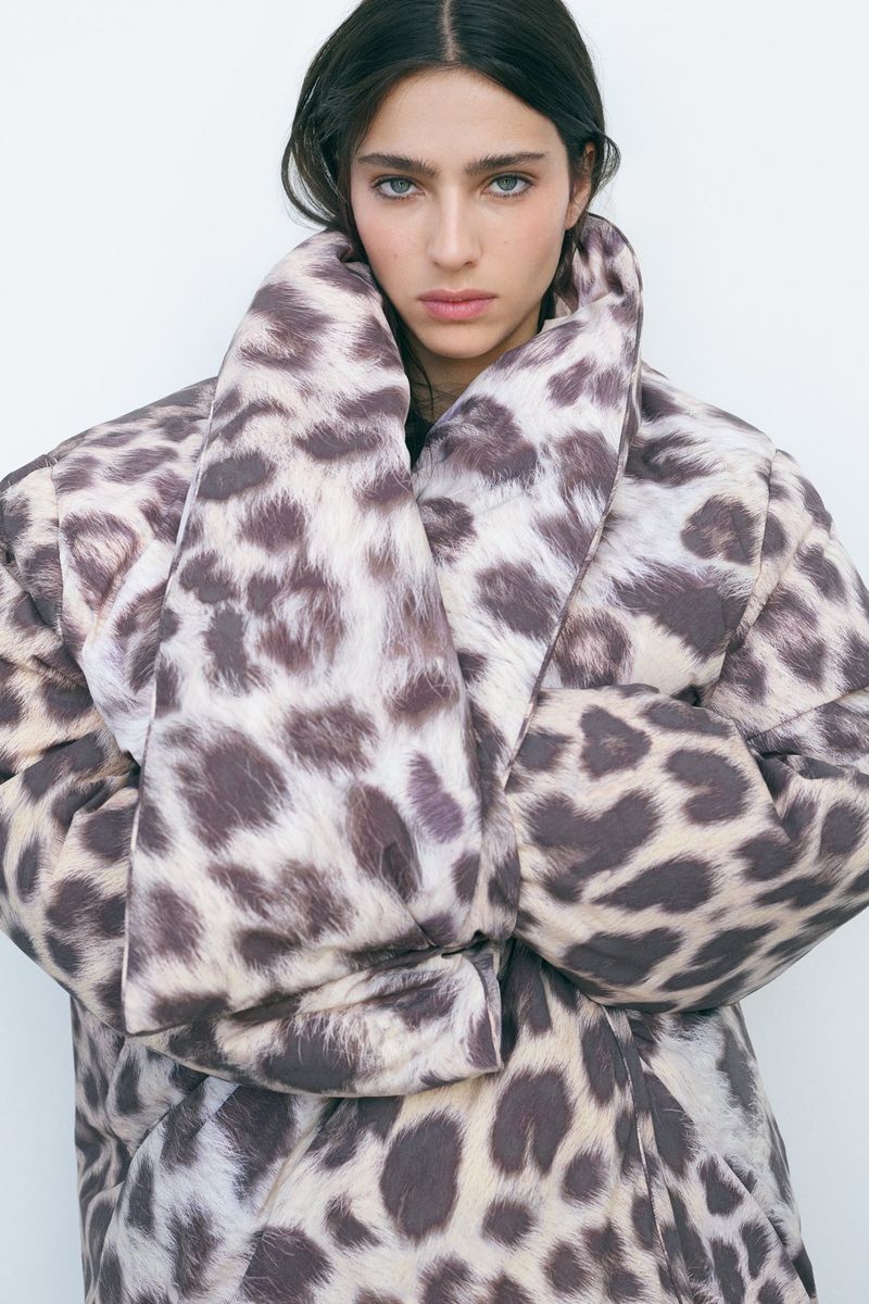 Model Loli Bahia posing in an oversized leopard print puffer coat against a plain white studio background.