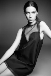 Model Loli Bahia wearing a dark sleeveless dress against a neutral grey studio backdrop in a black and white fashion lookbook photograph.
