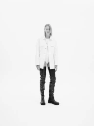 Model Annely Bouma wearing a white jacket and black thigh-high boots against a plain white background for ADELBEL SS25