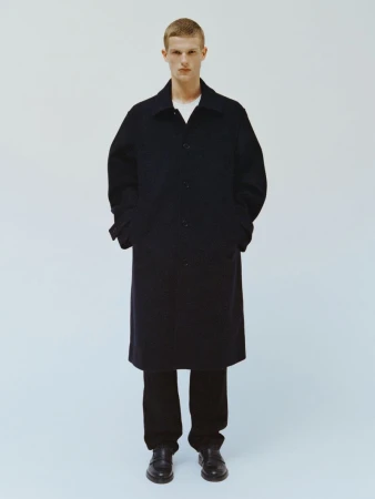 Full-length shot of a fair-skinned adult male in an overcoat, trousers, and dress shoes, posing in a bright photo studio against a light blue backdrop.