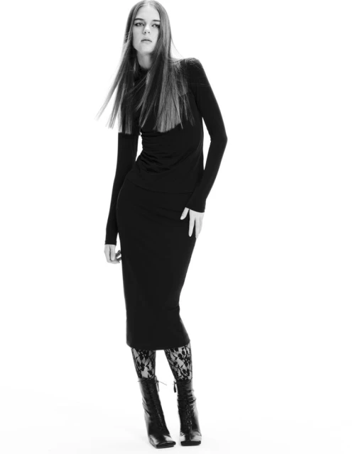 Full-length portrait of a woman with long hair, wearing a black dress and lace boots, against a white background in a studio setting.