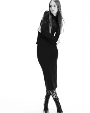 Model Tilda Jönsson wearing a black long-sleeve top and skirt with patterned tights against a white seamless background