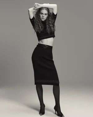Model with long curly hair wearing a black crop top and matching skirt posing against a seamless grey studio background