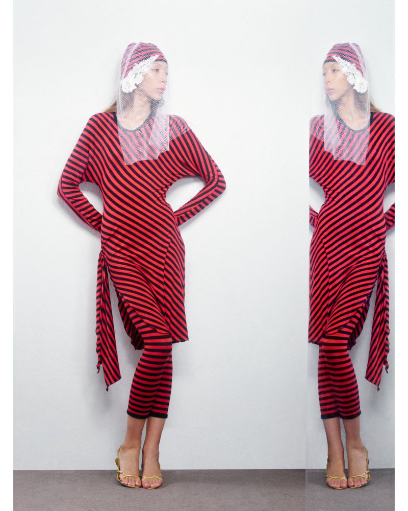 Woman in a red and black striped dress and head covering poses indoors in front of a reflective surface, displaying the outfit.