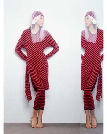 Woman in a red and black striped dress and head covering poses indoors in front of a reflective surface, displaying the outfit.