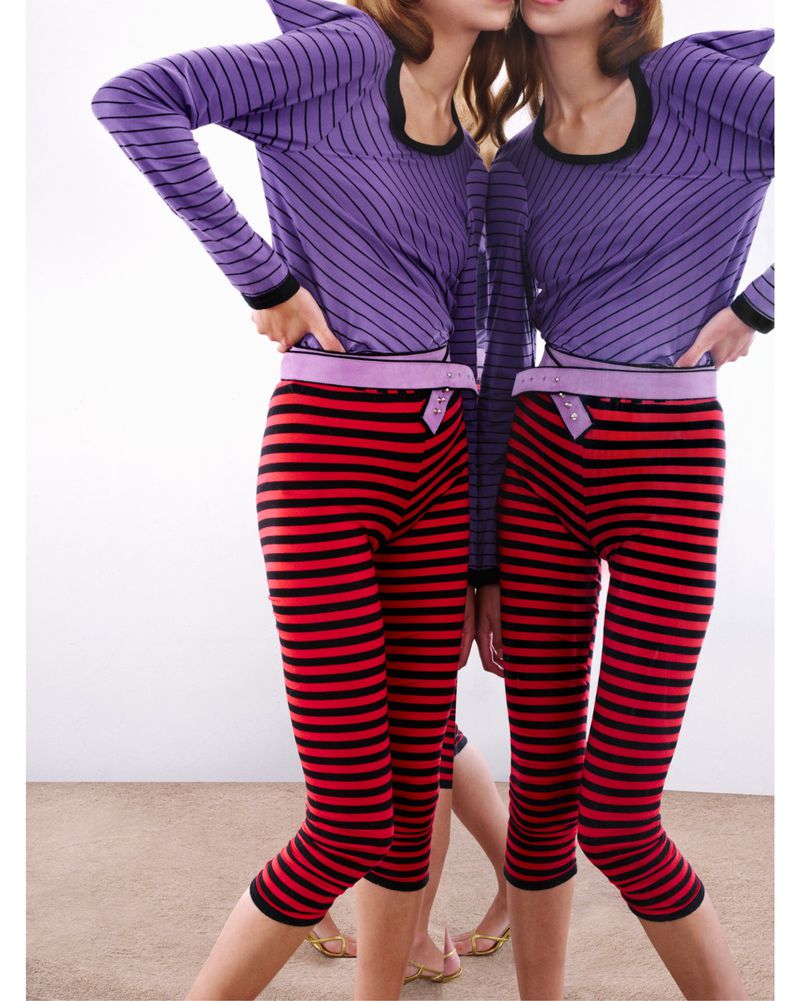 Two models pose indoors wearing matching striped tops and capri pants in a fashion forward photo. White background and tan flooring.