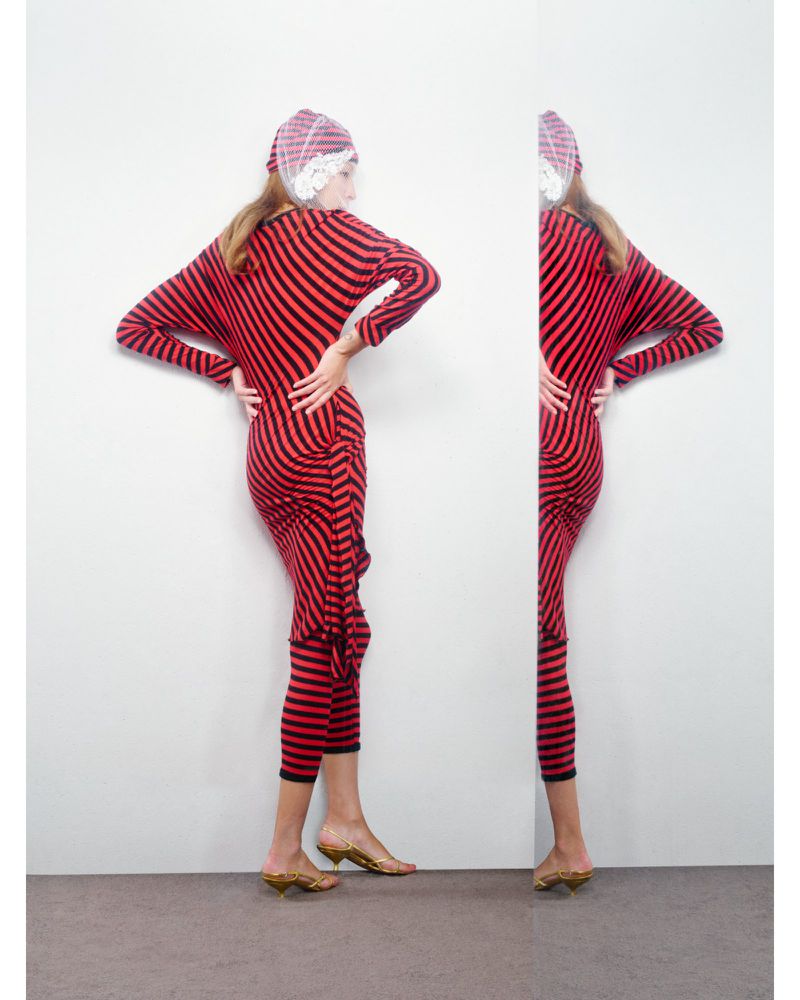 Fashion shot of a woman in a red-and-black striped outfit with hands on hips, split image with a mirror effect against a white wall.