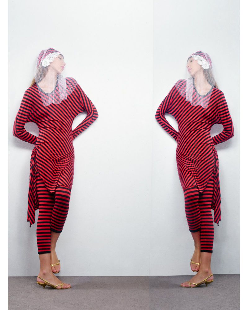 Two adult females mirroring in a studio portrait, wearing a red and black striped dress, sheer white floral bonnet, and gold kitten heels.