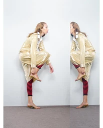 Model wearing a shiny gold coat and red-striped leggings adjusting a sandal against a neutral backdrop