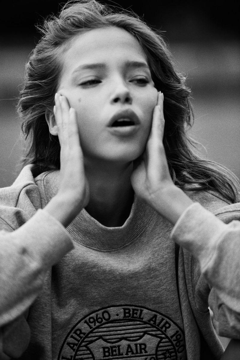 Black and white portrait of a young adult woman in a sweatshirt, holding her hands to her face with an open mouth expression.