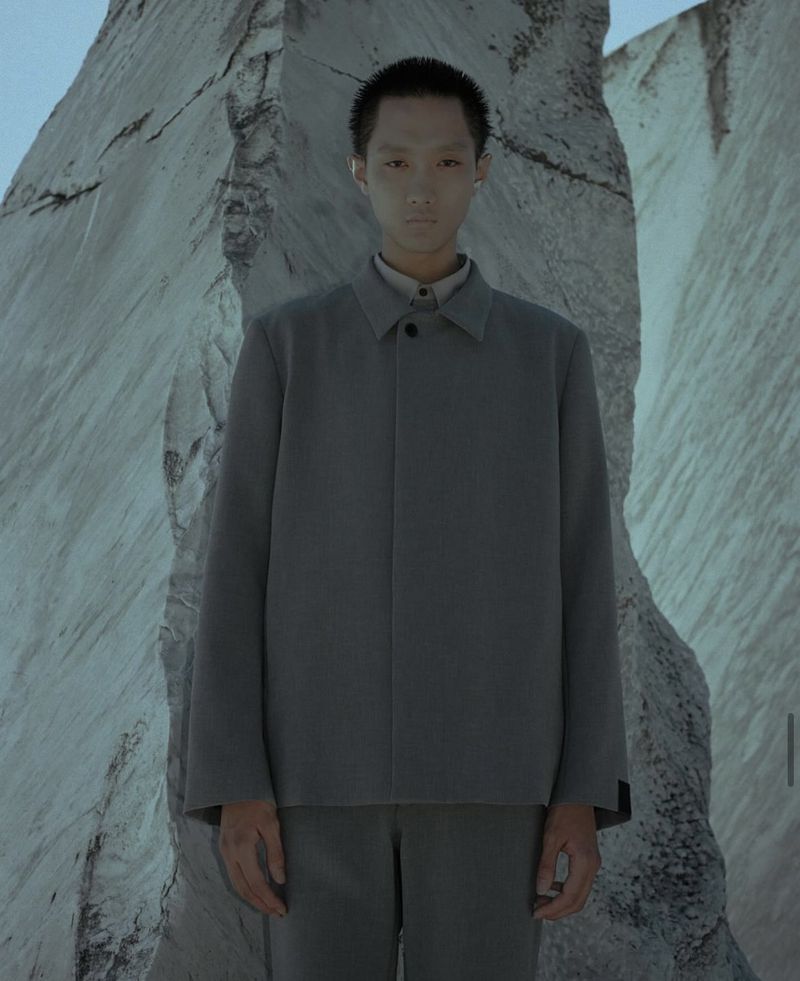 Portrait of androgynous person in grey suit with mountain stone background, low lighting. Fashion concept or visual art.
