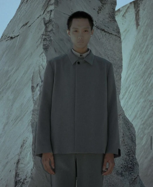 Portrait of androgynous person in grey suit with mountain stone background, low lighting. Fashion concept or visual art.
