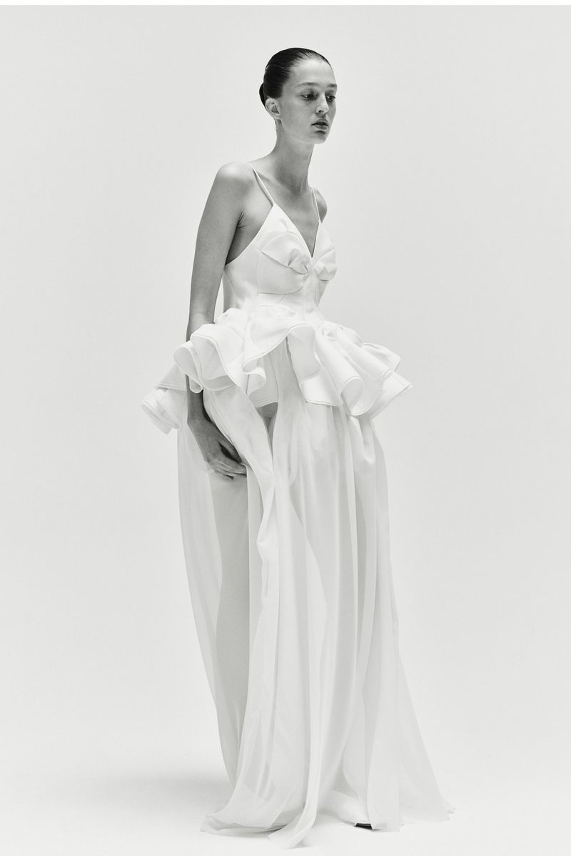 Elegant woman in a white gown poses in a studio setting, showcasing fashion and style in a minimalist, high-key image.