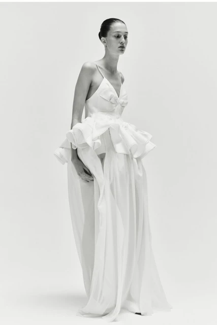 Elegant woman in a white gown poses in a studio setting, showcasing fashion and style in a minimalist, high-key image.