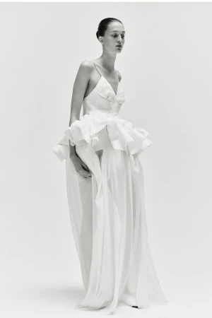 Elegant woman in a white gown poses in a studio setting, showcasing fashion and style in a minimalist, high-key image.