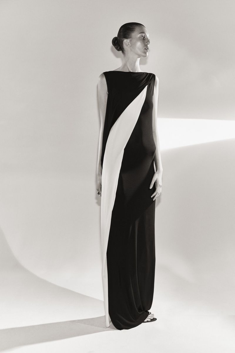 Elegant woman poses in a full-length black and white gown in a studio with a soft, diffused lighting that accentuates the dress's design.