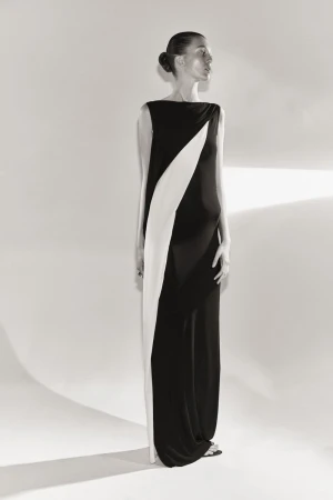 Elegant woman poses in a full-length black and white gown in a studio with a soft, diffused lighting that accentuates the dress's design.