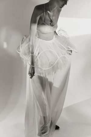 Model wearing a white sculptural tulle skirt with circular structural wire and sheer halter top against a light studio backdrop.