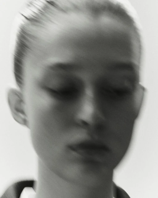Close-up black and white portrait of a young adult female with a blurred motion effect, showcasing her delicate features and smooth skin.