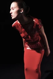 Model wearing a red textured top and red skirt posing against a dark background for the Ashlyn S/S25 lookbook.