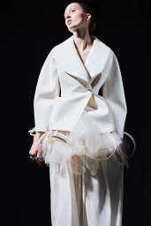 Model wearing structured white jacket and layered tulle skirt against a solid black background for Ashlyn SS25 lookbook.