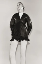 Model wearing a black leather jacket and white tights against a neutral background for Ashlyn SS25 lookbook