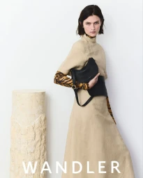 Model wearing a beige dress and animal-print top holding a black handbag in a minimalist white studio setting
