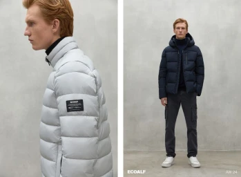 Red-haired male model wearing a quilted puffer jacket and turtleneck against a minimalist concrete studio wall