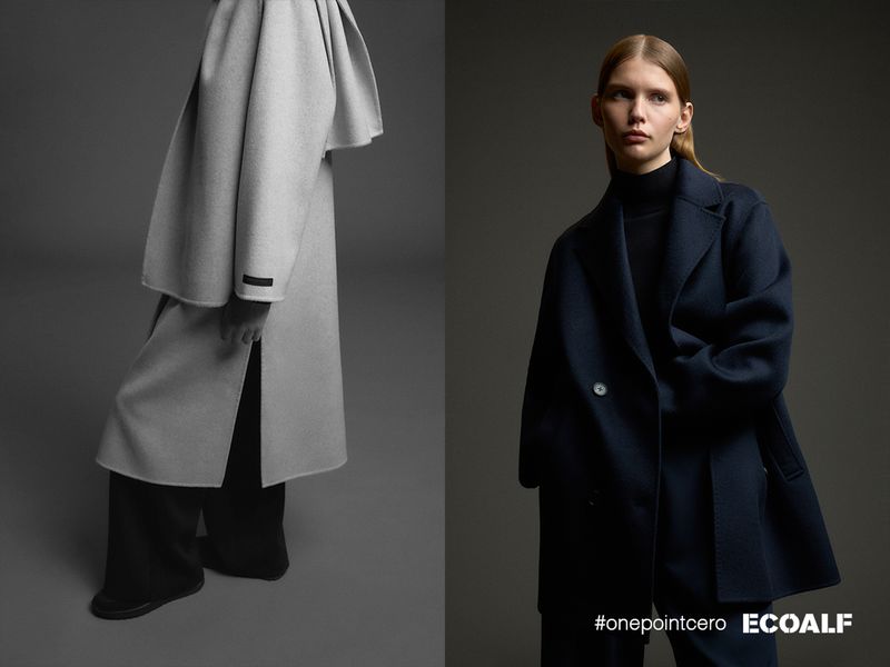 Fashion editorial shot against grey backdrop featuring an adult woman in a navy coat and a grey coat. Minimalist clothing in a studio.
