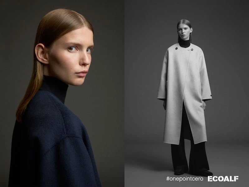 Fashion editorial shot of a young adult woman in a dark blue sweater and a long light grey coat, photographed in a photo studio setting.