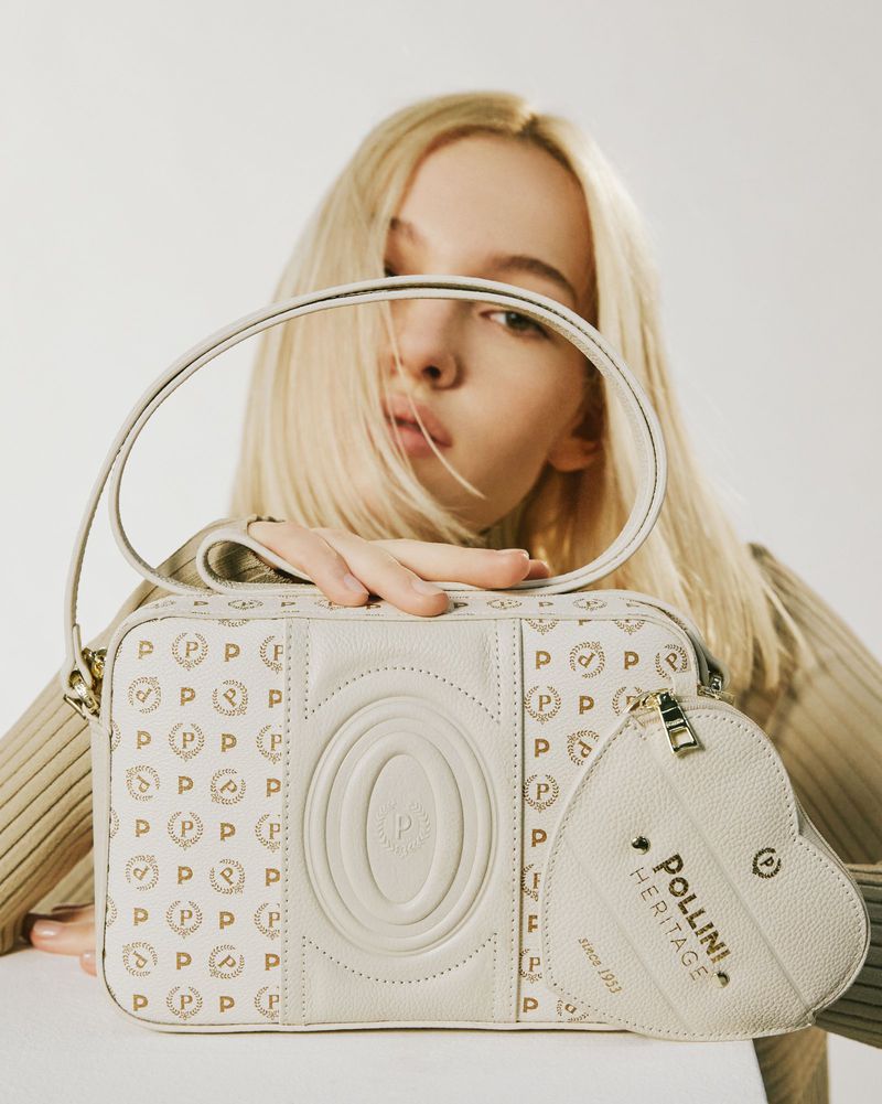 Close-up studio shot of a young fair-skinned adult woman holding a white Pollini handbag with a matching heart-shaped coin purse.