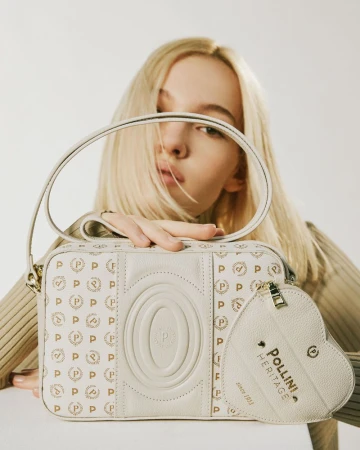 Close-up studio shot of a young fair-skinned adult woman holding a white Pollini handbag with a matching heart-shaped coin purse.