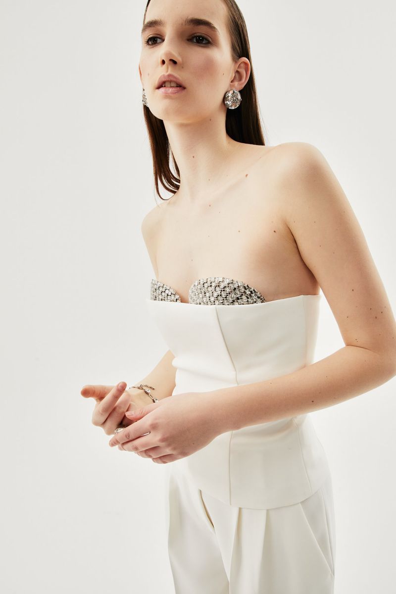 Elegant adult woman in a strapless white top and matching pants poses in a bright studio with natural-looking make-up.