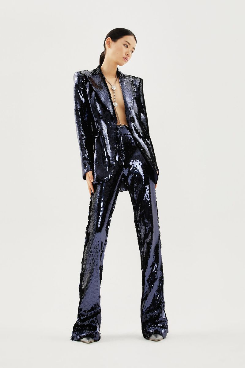 An Asian female model poses in a shimmering navy blue sequined suit against a white background. The outfit includes a blazer and flared trousers.