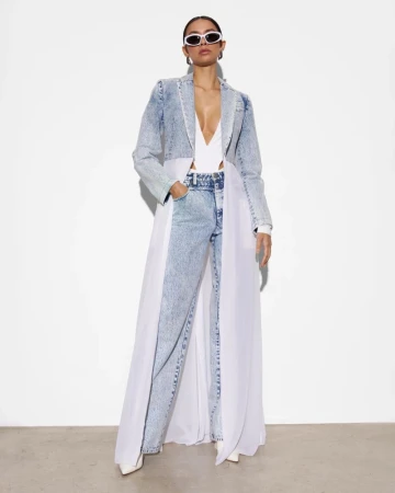 A woman poses in a denim coat and jeans with white sheer accents, complemented by white sunglasses and pointed heels against a white backdrop.
