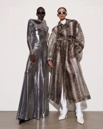 Two fashion models posing in sunglasses, one in a metallic silver gown and the other in a snakeskin print trench coat.