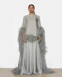 Model wearing a floor-length silver satin gown with voluminous grey feather trim against a white studio background.