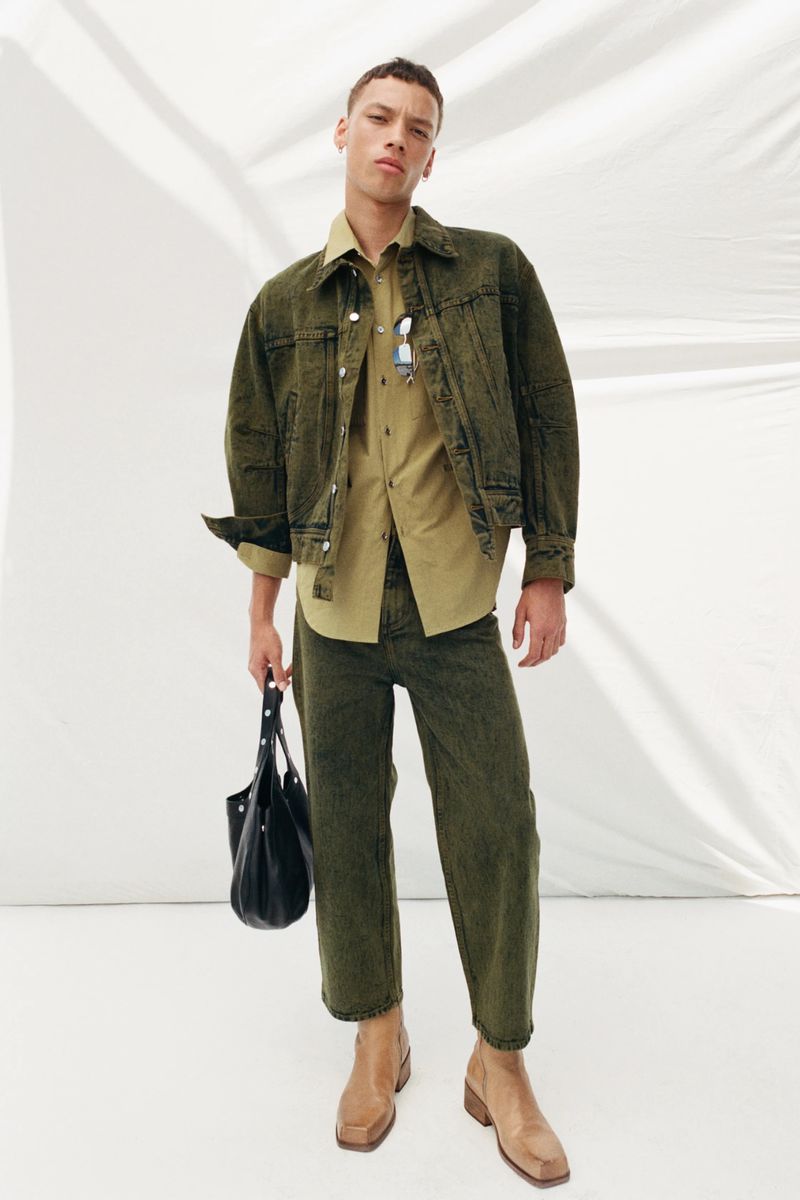 A full-length studio shot features a male model in a green denim jacket and jeans, paired with a tan shirt, boots, and a black tote bag.