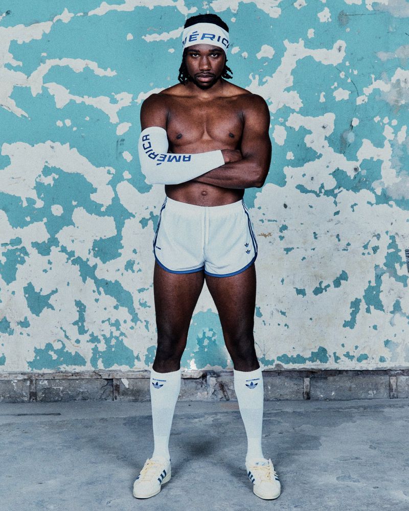 Athletic man in retro shorts and headband standing in front of textured wall. White socks and sneakers complete the vintage look.
