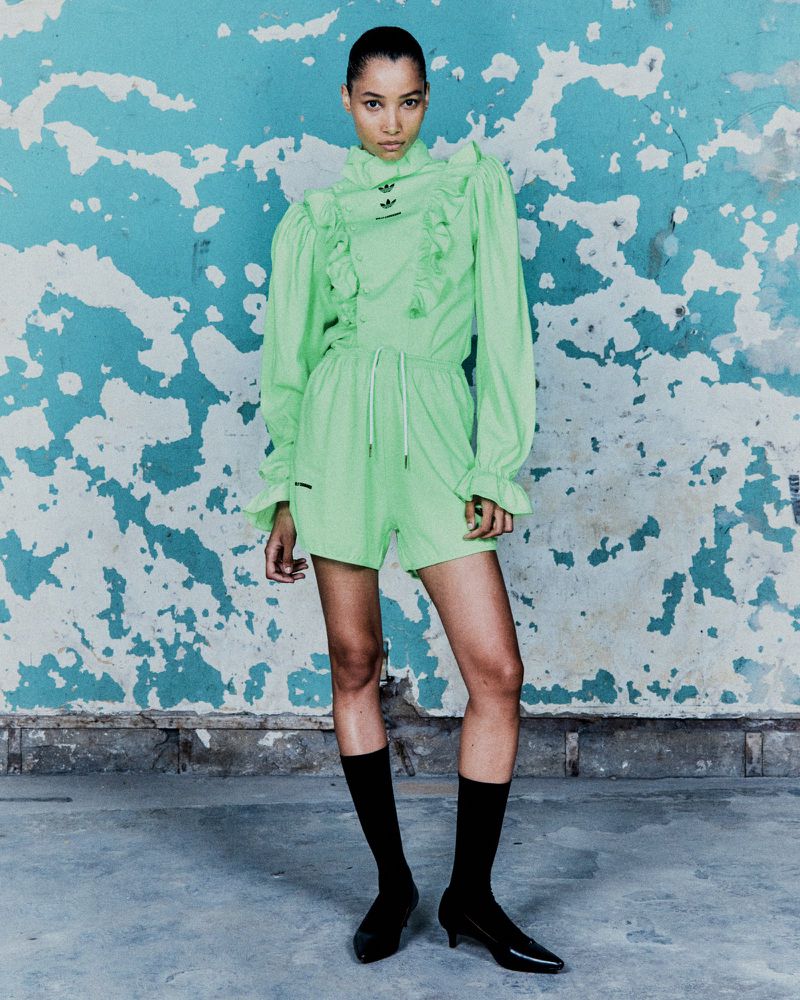 Elegant young woman in a lime green Adidas outfit poses confidently against a distressed blue and white wall, showcasing a high-fashion style.