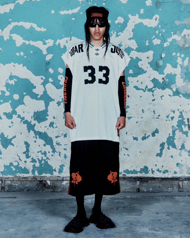 Person in a white jersey with the number 33, black skirt with orange floral details, black sunglasses, and a black bandana.