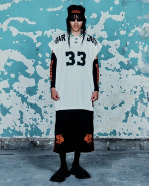 Model wearing a white mesh jersey with the number 33 and black shorts against a distressed blue wall for Willy Chavarria S/S 25.