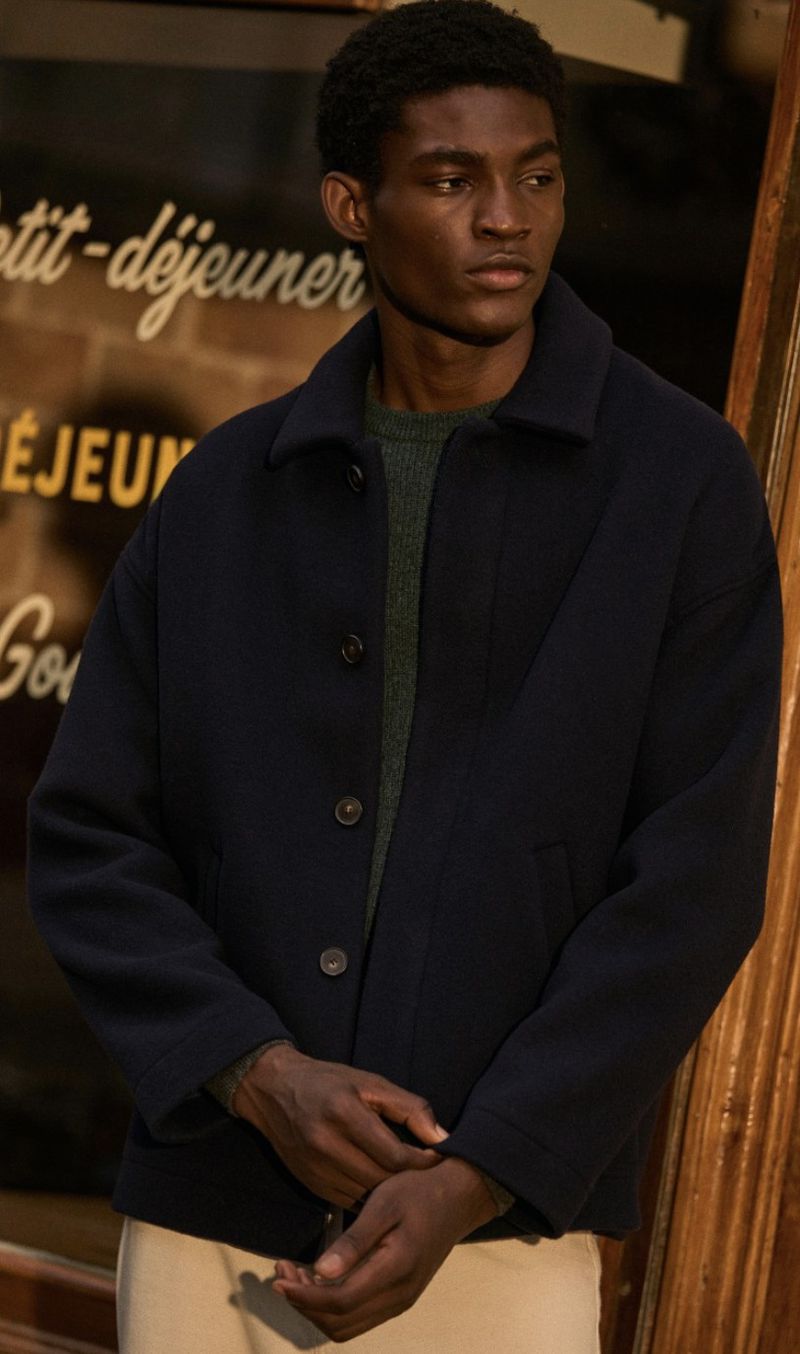 Portrait of African American man in navy jacket in front of building with French signage; fashion, lifestyle, and beauty concept.