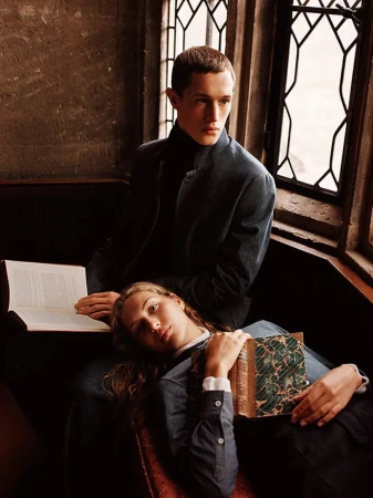 Two people in a naturally lit corner; a seated man and a reclining woman with a book in her lap. Interior setting with warm, muted colors.